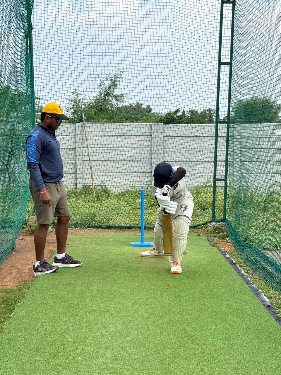 Young batter practicing in the cricket nets with a coach